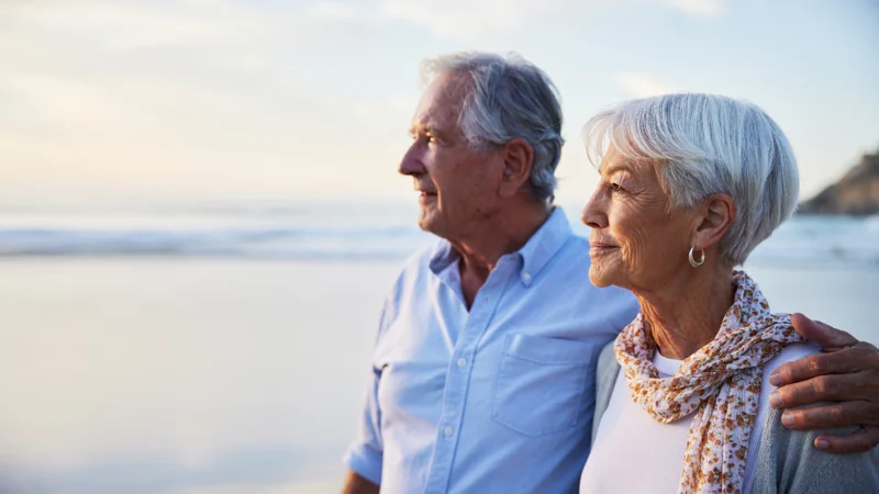 Senior couple looking at the view while standing on a beach at sunset