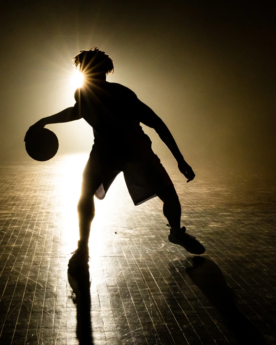 A silhouette of a basketball player backlight by a strong light. - For professional athletes